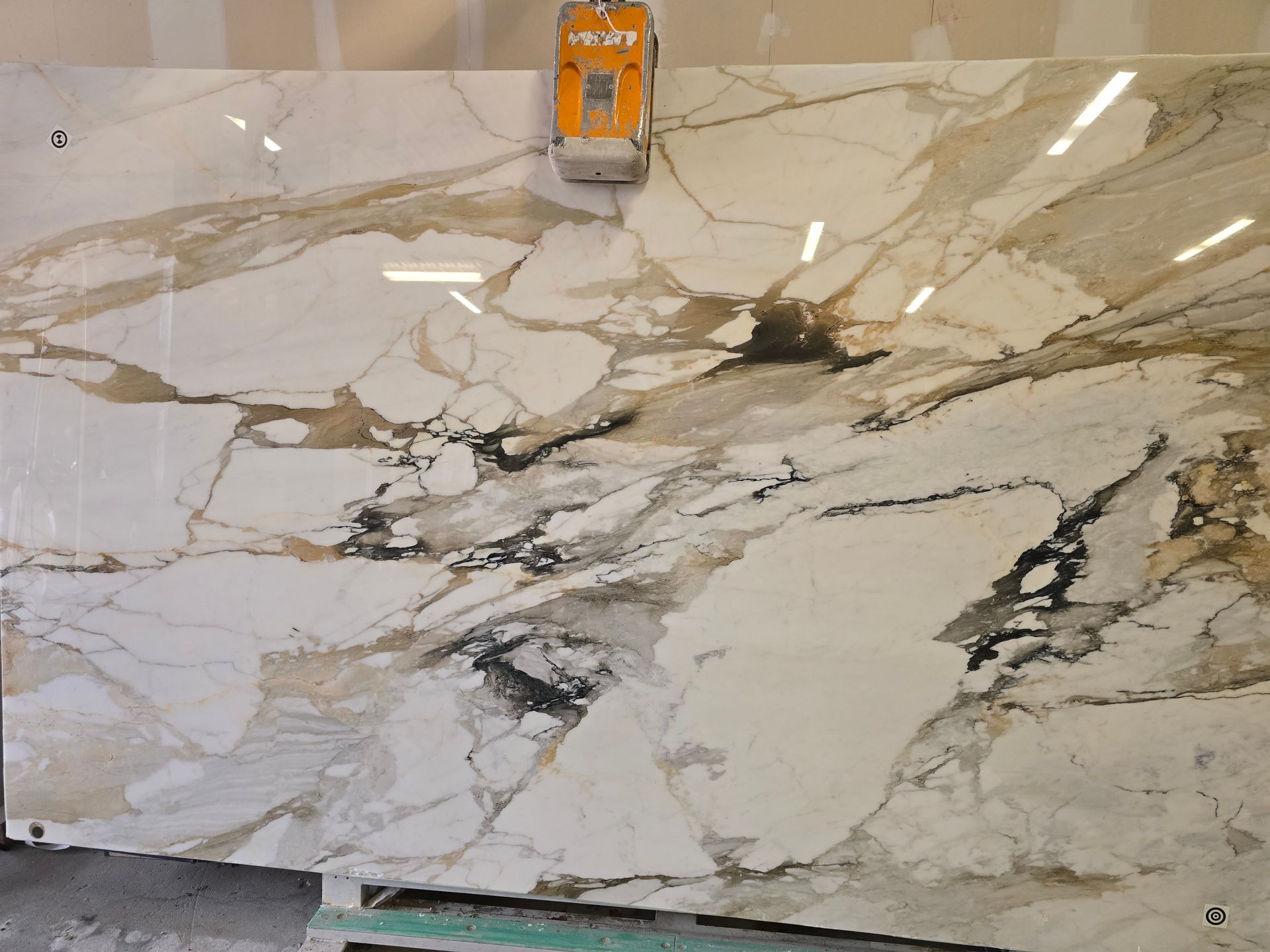 Large slab of white and gold marble with black veining, being cut by a yellow machine.