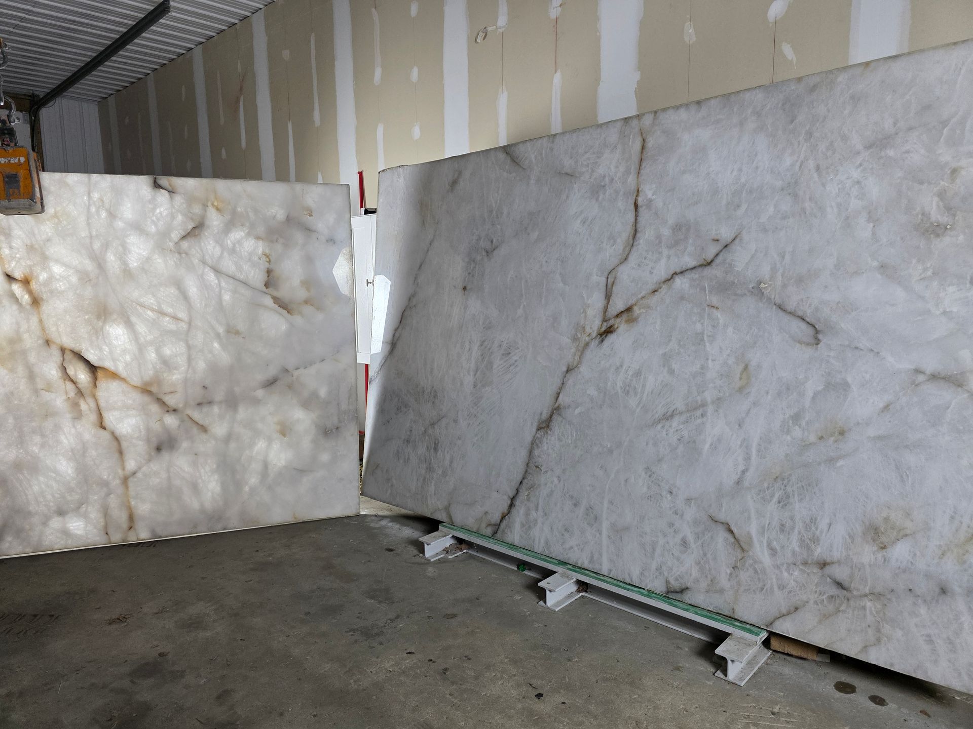 Two large, light-colored stone slabs with brown veining, leaning against a wall in a warehouse.
