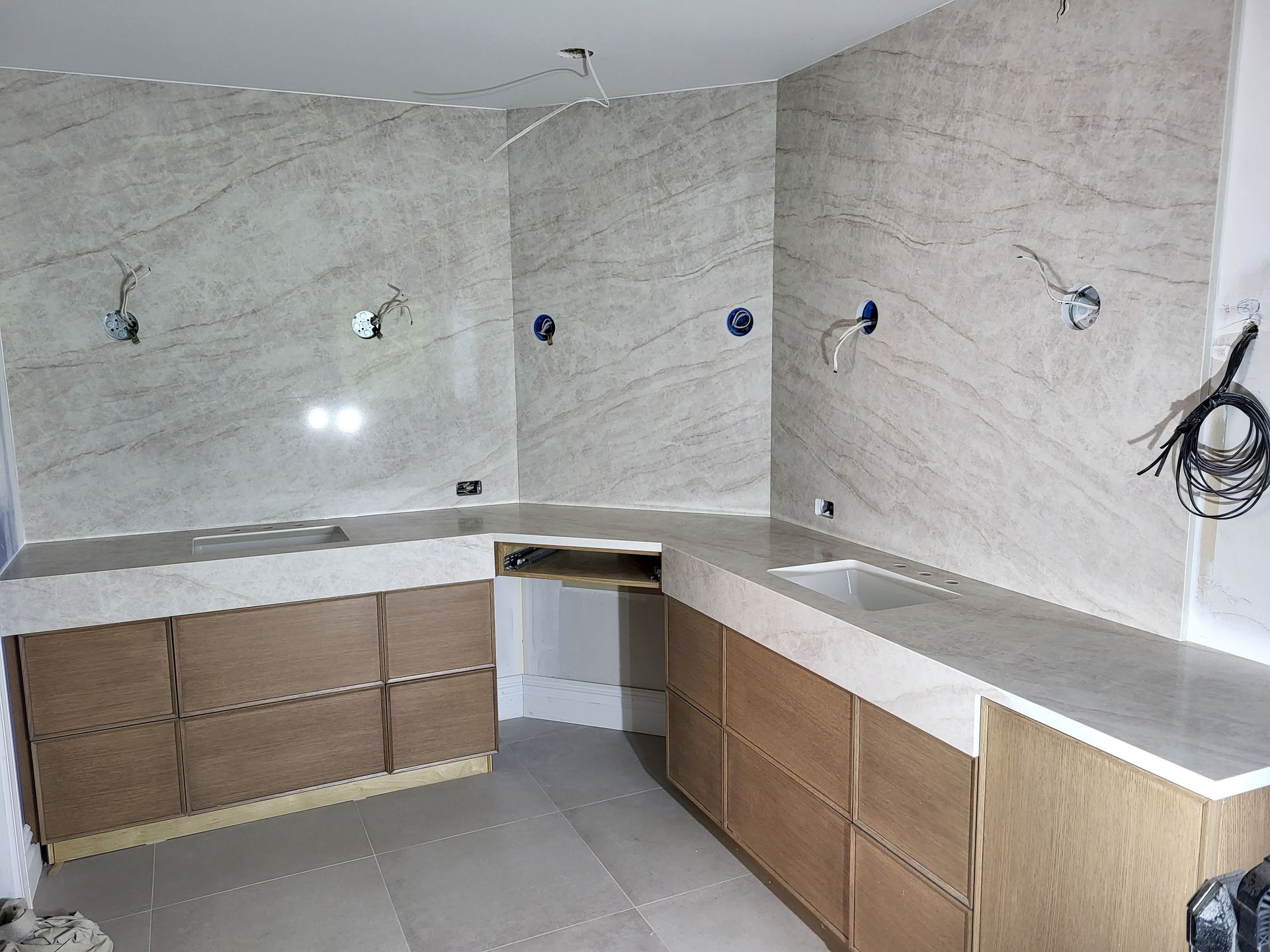 Kitchen under construction with beige countertops, light wood cabinets, and light beige stone wall tiles.