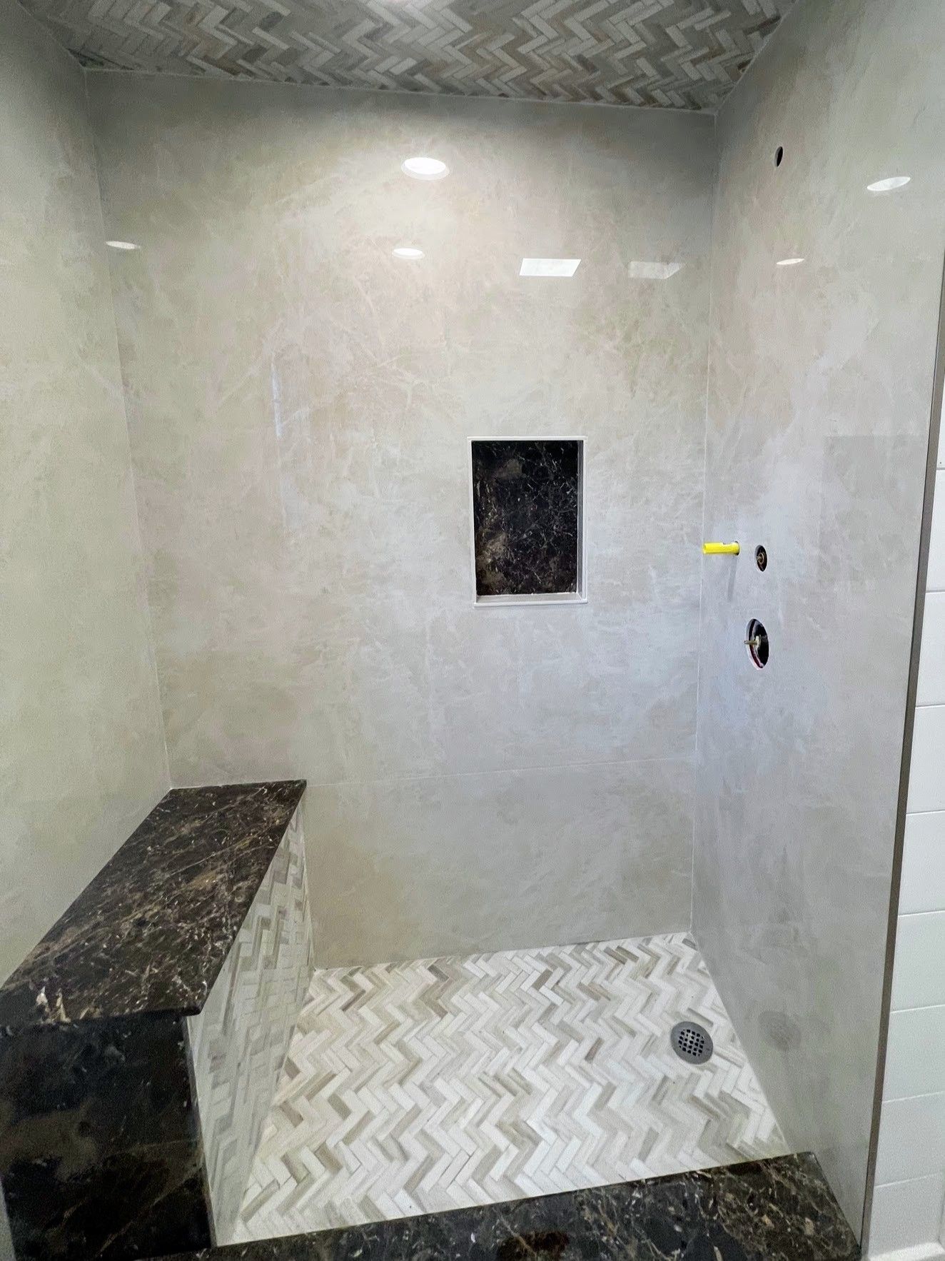 Shower with gray and patterned tile, built-in bench, dark granite trim, and a recessed shelf.