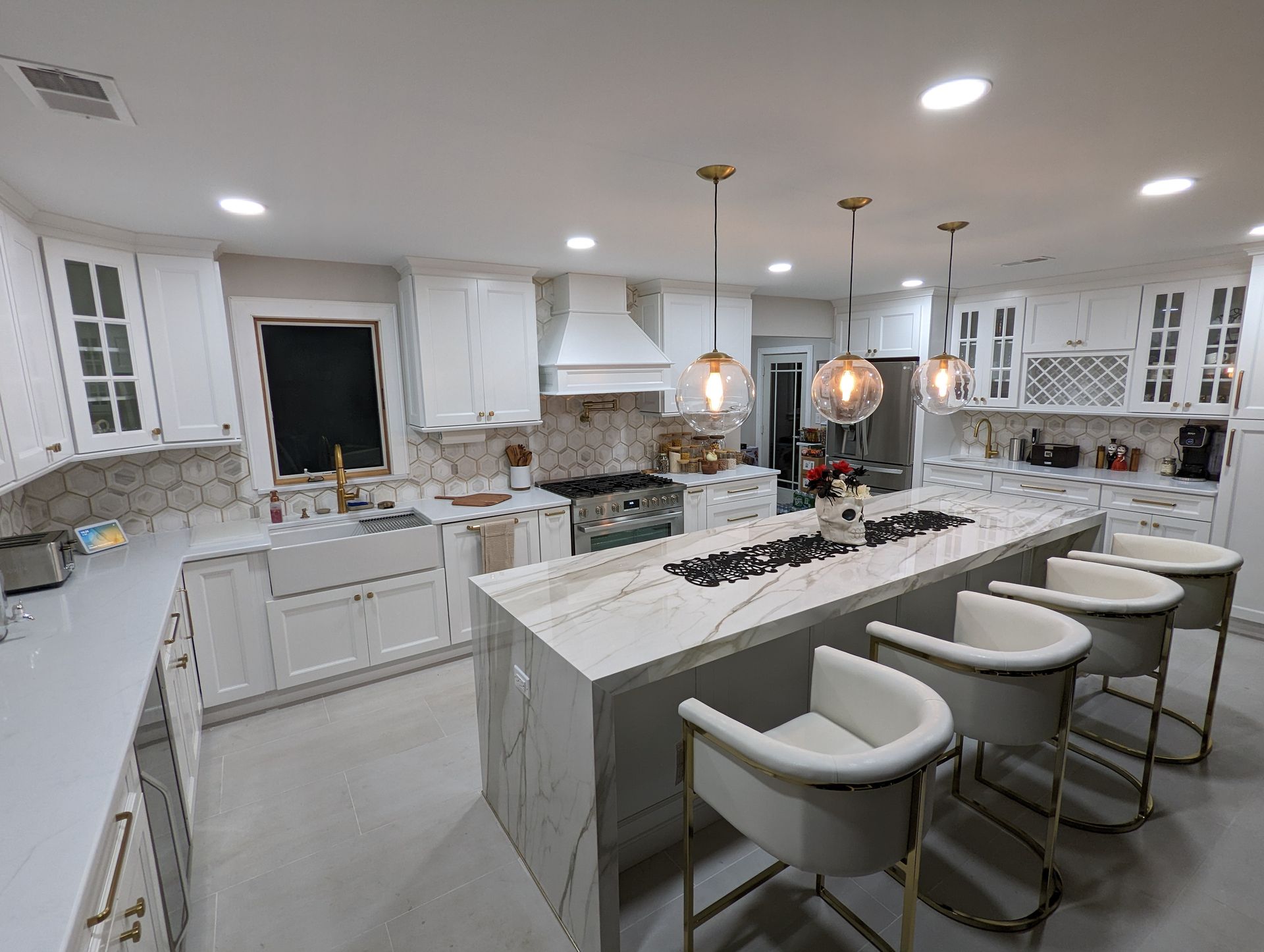 White kitchen with island, marble countertops, pendant lights, and bar stools.