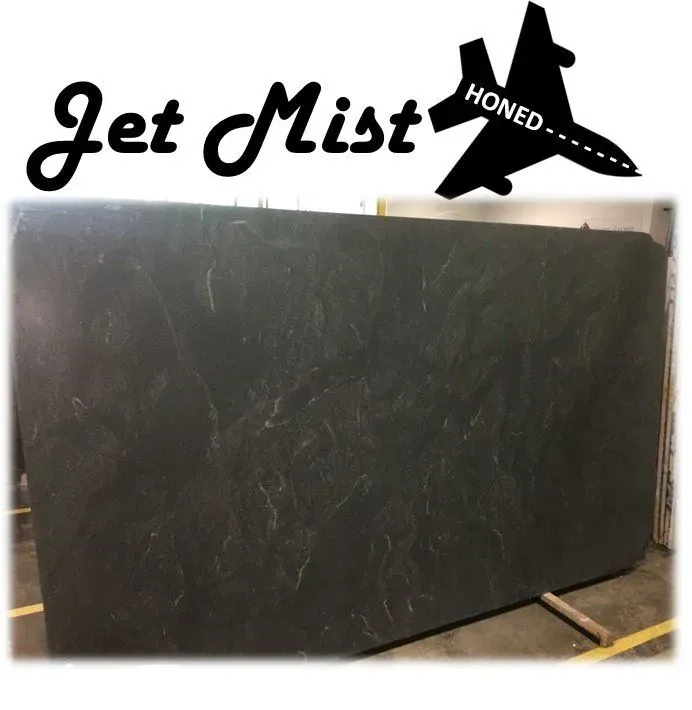 Large slab of dark gray Jet Mist Honed granite. Logo includes a jet silhouette.