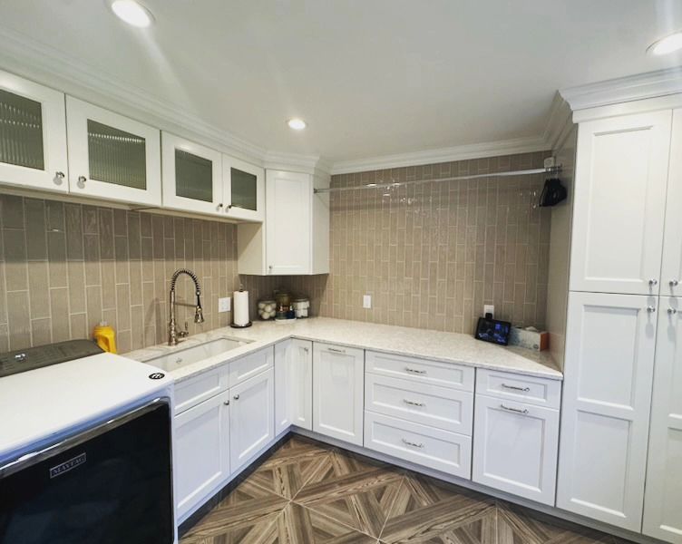 A well-lit laundry room with white cabinets, light countertops, and a beige tiled backsplash.