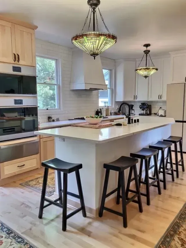 Kitchen with white cabinets, island with stools, and stained glass pendant lights.
