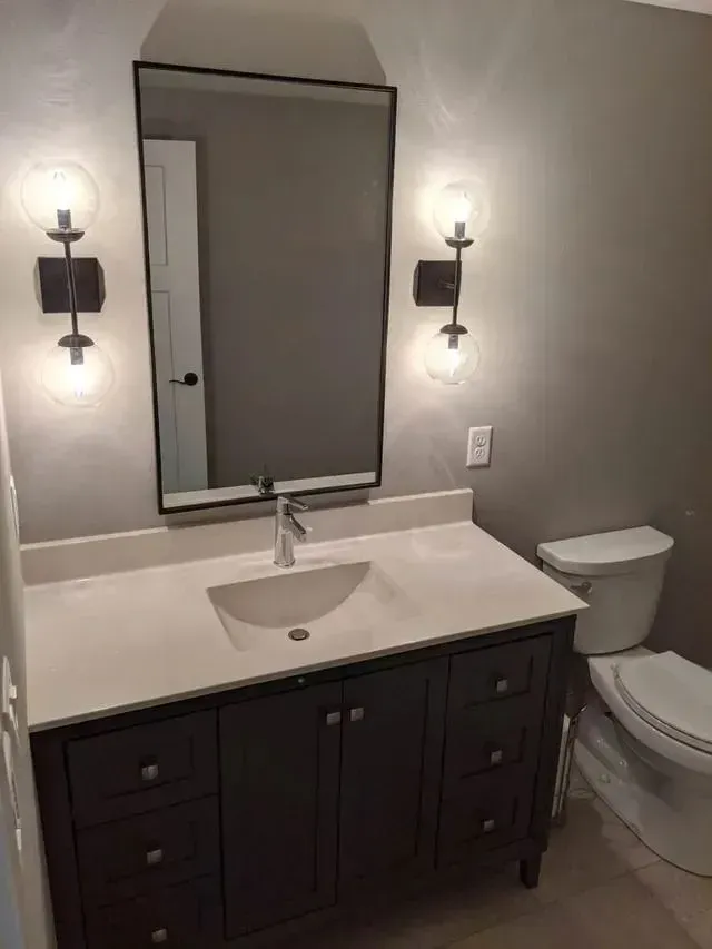 Bathroom with a dark vanity, a white countertop, a mirror, and sconce lights.