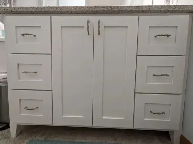 White bathroom vanity with drawers and doors, gray countertop, silver handles.