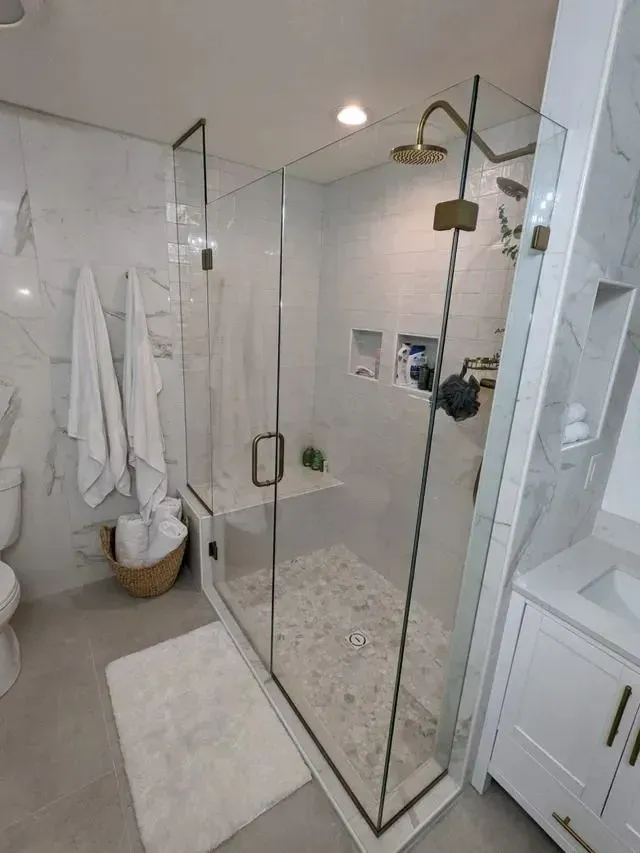 Modern bathroom with marble tile, glass shower, and gold fixtures.