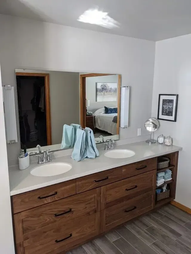 Bathroom with dual sinks, wooden vanity, large mirror, towels, and gray countertops.