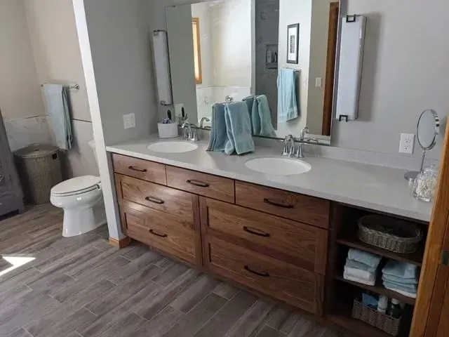 Bathroom with double vanity, light gray countertop, wood cabinets, mirrors, and pale blue towels.