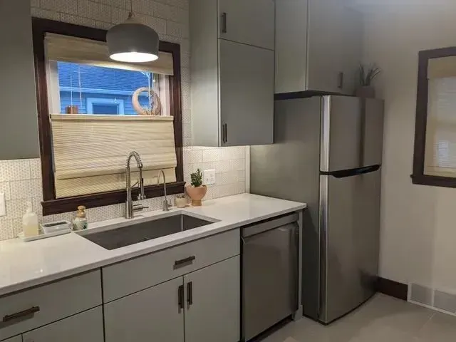Modern kitchen with light green cabinets, stainless steel appliances, and a window above the sink.