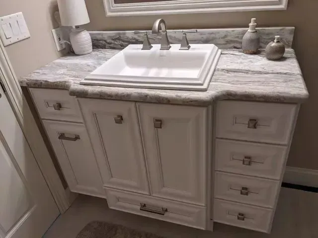 White bathroom vanity with marble countertop, sink, and drawers.