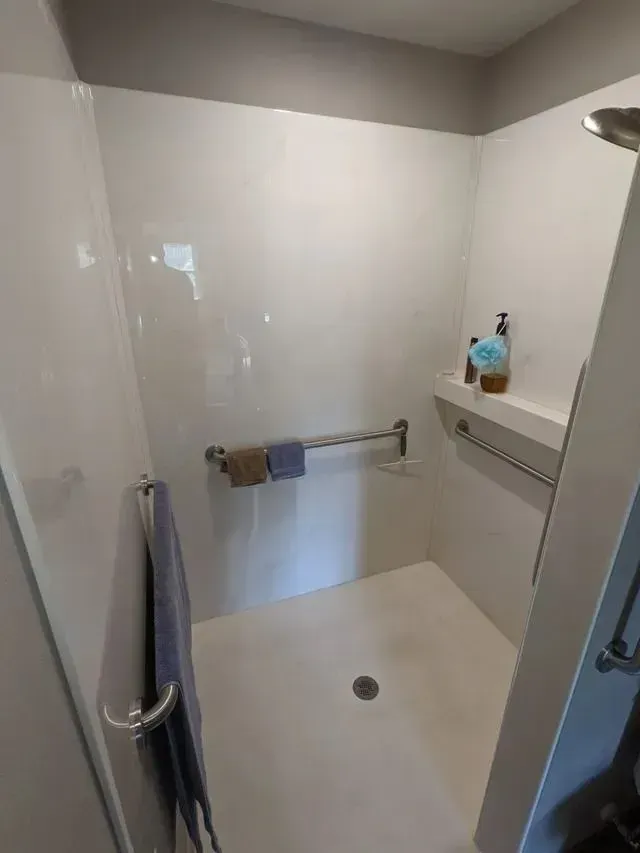 White accessible shower with grab bars, towels, and a shelf for toiletries.