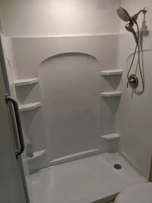 White shower stall with shelves, arched wall niche, and handheld showerhead.