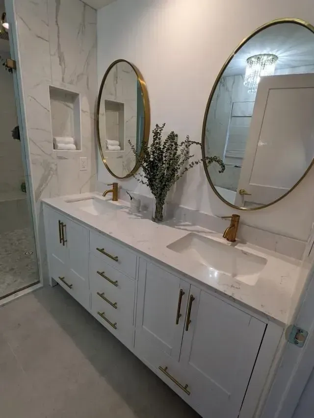 White bathroom vanity with two sinks, gold fixtures, and oval mirrors.