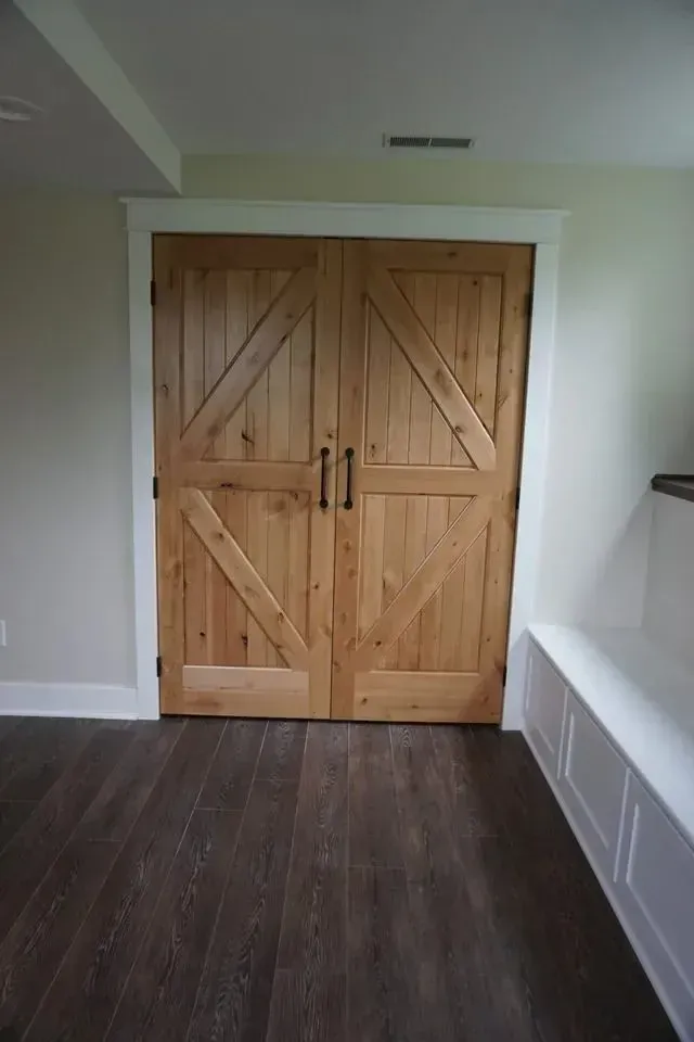 Wooden barn doors with dark handles, white trim, on wood-look floor, adjacent to a built-in white bench.