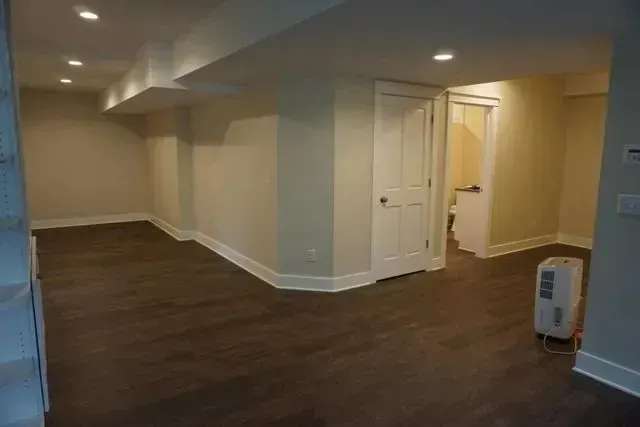 Finished basement with beige walls, dark flooring, and a closed white door.