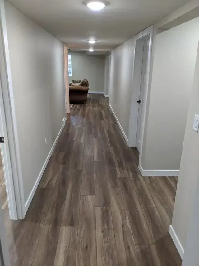 Long hallway with wood-look flooring, gray walls, and white trim. A door and a couch are visible.