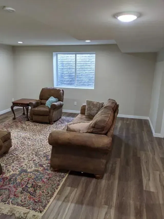 A living room with brown furniture on a patterned rug and wood-look flooring. A small table sits next to a recliner.