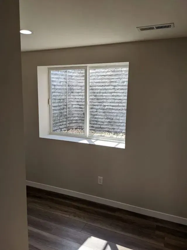 Room with a window, tan walls, and dark flooring. Window looks into a well.