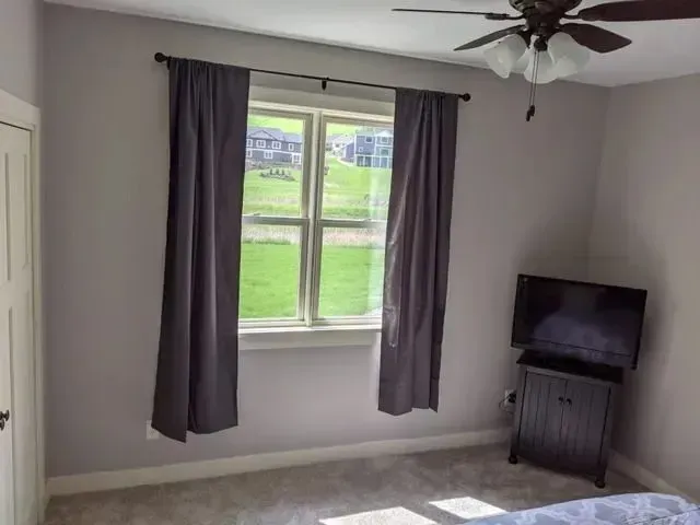 Bedroom with window and gray curtains, TV on stand, neutral walls, and light carpet.