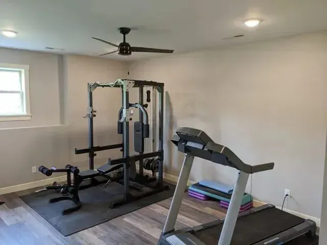 Home gym with weight machine, bench, treadmill, step platform, and ceiling fan.