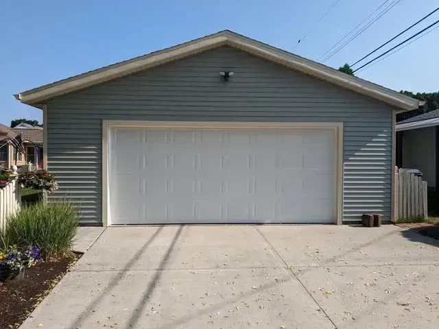 A light blue garage with a white garage door, set in a concrete driveway, against a clear sky.