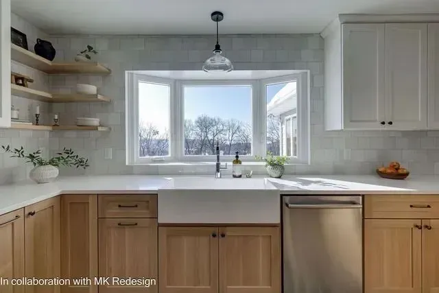 Modern kitchen with light wood cabinets, white countertops, and bay window.