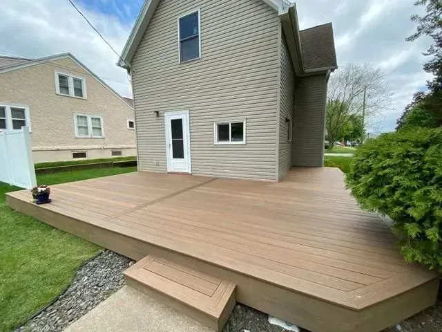Back of a two-story beige house with a brown composite deck and steps. Green lawn on either side.