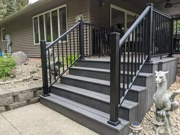 Black railing surrounds gray deck with steps leading up to house.