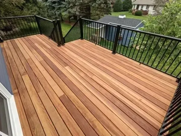 Wooden deck with black metal railing, overlooking a yard with a house.