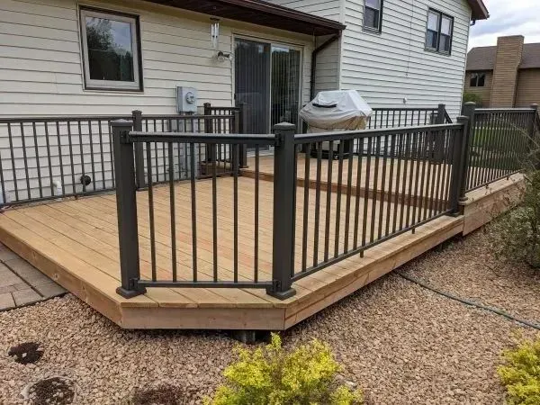 Wooden deck with black metal railing, adjacent to a house with sliding glass door.