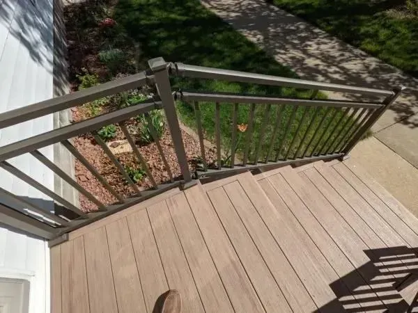Composite deck with brown railing and stairs, next to landscaping and a sidewalk.