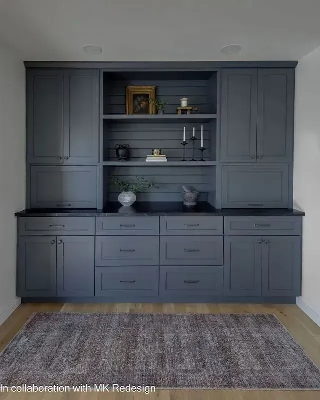 Gray built-in cabinets with open shelves and countertop, decorated with objects, over a rug on hardwood floor.