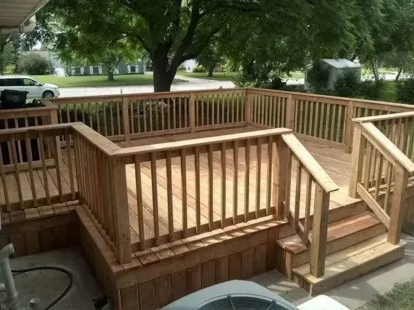 Wooden deck with railings and stairs, built onto a house, with green yard in background.