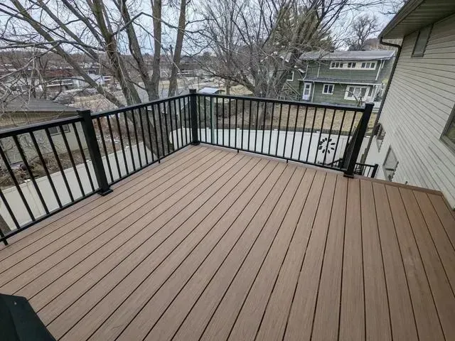 Brown composite deck with black metal railing overlooking a yard and houses.
