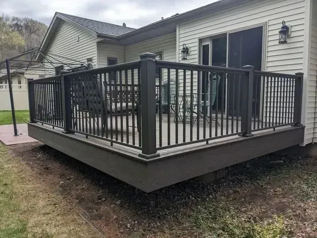 Gray composite deck with black railing and patio furniture next to a light-colored house.