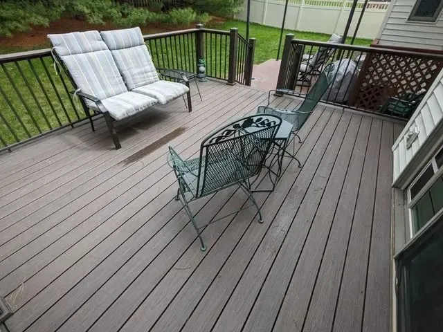 Deck with gray composite decking, black wrought iron chairs and couch with striped cushions.