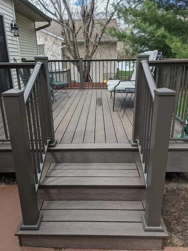 Deck with steps, brown composite boards, gray railing, leads to seating area, backyard setting.