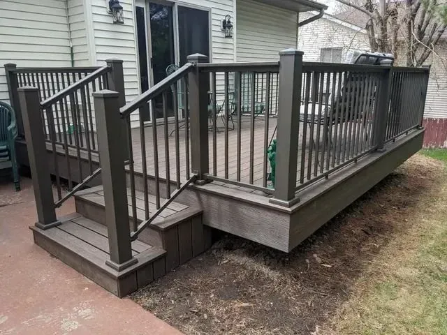 A wooden deck with dark railing and steps, leading to a sliding glass door.