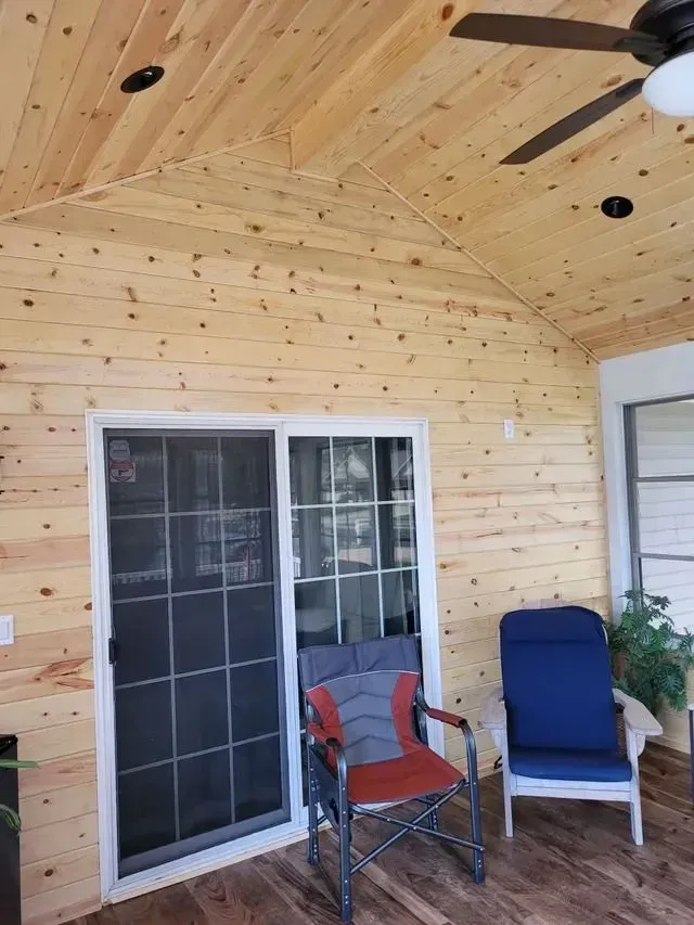 Enclosed porch with wood paneling, sliding door, chairs, and ceiling fan.