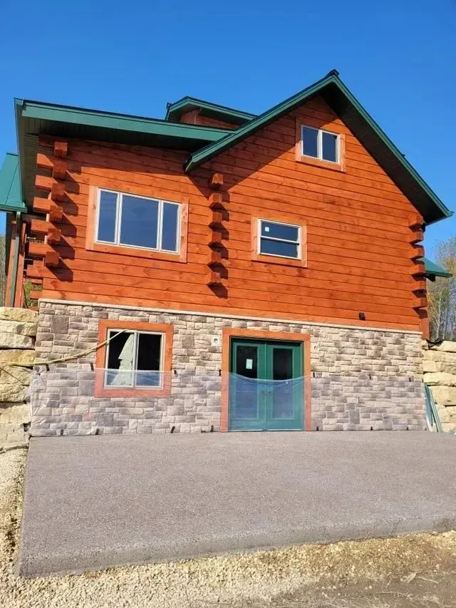 Two-story log cabin with stone foundation, green roof, and blue sky.