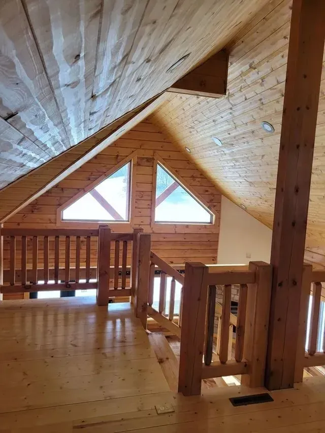 Wooden interior with a loft, triangular windows, and a railing.
