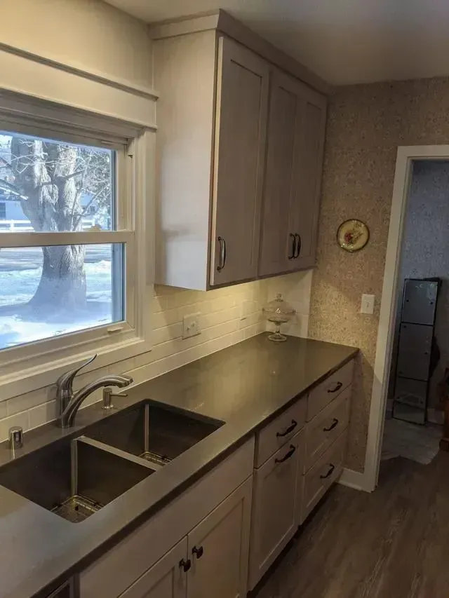 Kitchen with gray cabinets, dark countertop, and stainless steel sink. Window on left.