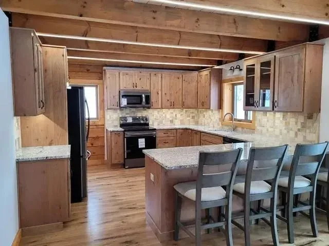 Kitchen with wooden cabinets, island with stools, and appliances, with wood beams overhead.