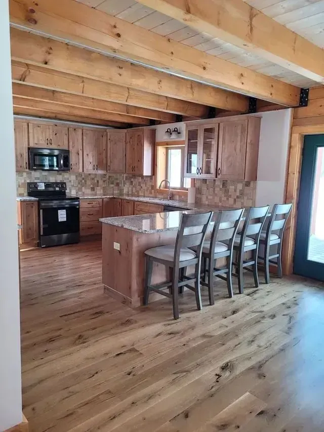 Kitchen with wooden cabinets, island with seating, stone backsplash, and hardwood floors.