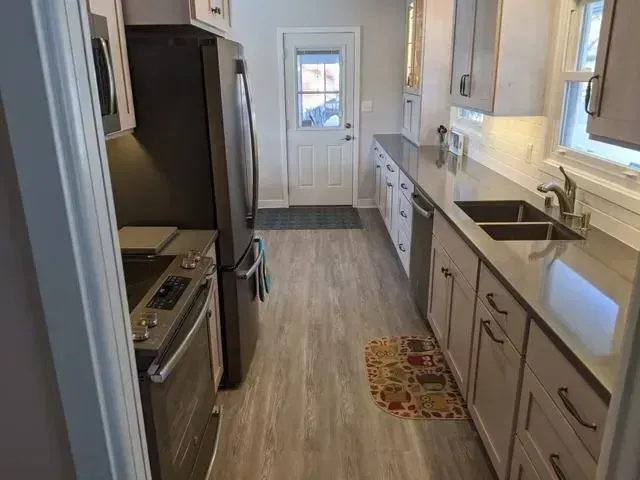 Kitchen with light wood-look flooring, light gray cabinets, dark countertops, and stainless steel appliances.