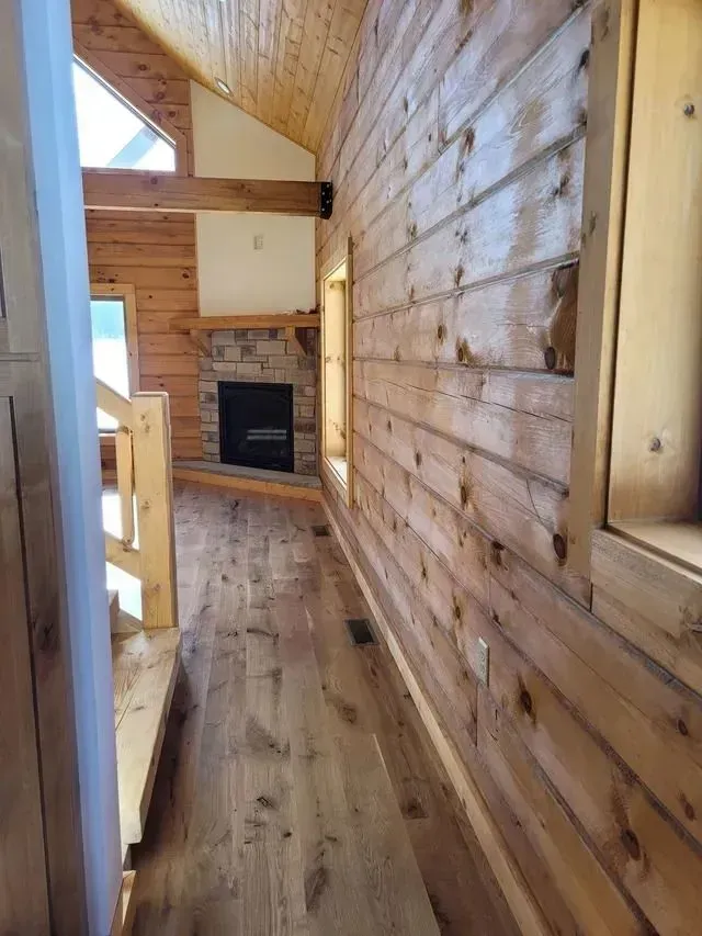 Wooden cabin interior with a fireplace, hallway, and wood plank walls.