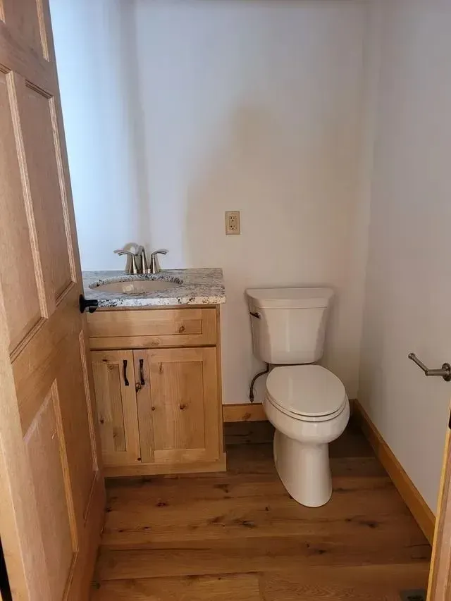 Small bathroom with a toilet, sink, and wood cabinetry. Light wood flooring and white walls.
