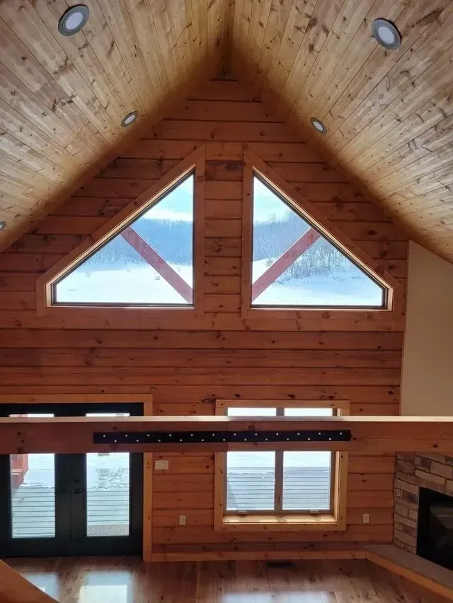 Wooden interior with triangular windows, exposed beams, and a view of snow.
