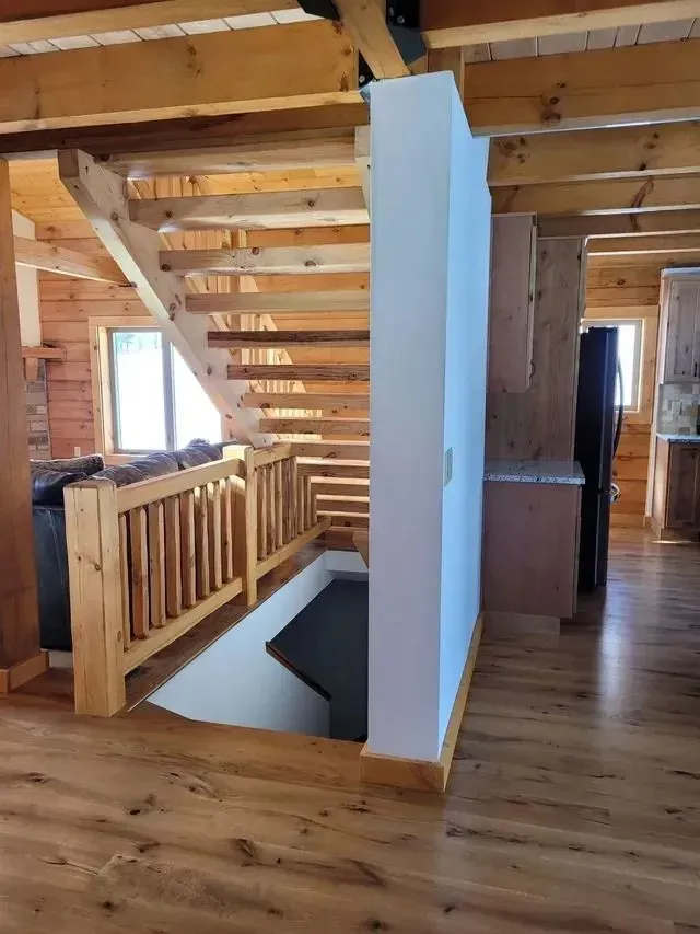 Wooden staircase leading down to a dark area, in a wood-paneled interior. Wooden handrail and white wall are present.